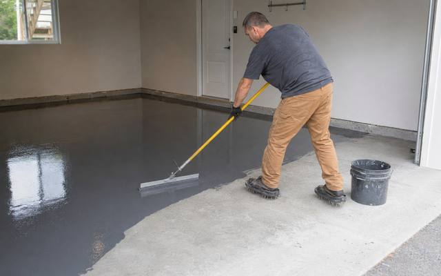 Installer rolling a grey coat onto a garage slab in Sherwood Park